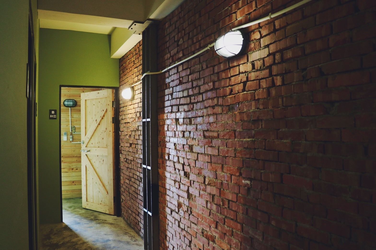 A hallway with a brick wall, a wooden door, and a light fixture.