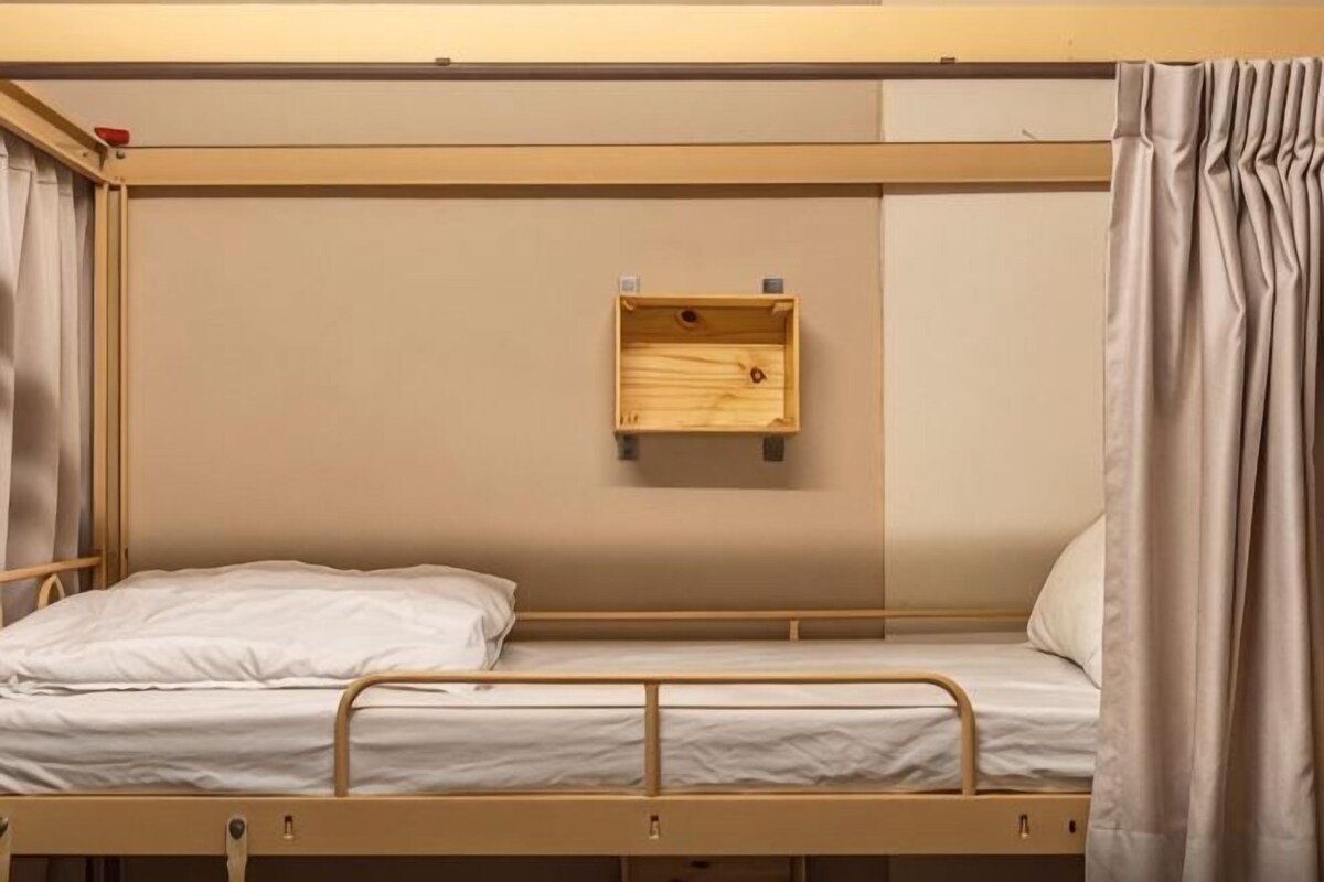 A bunk bed with a wooden shelf, curtains, and a metal frame.