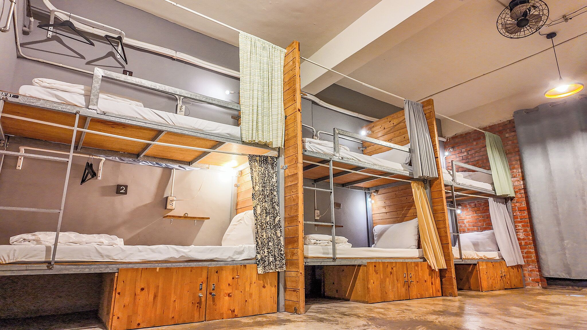 A dormitory-style room with bunk beds, wooden cabinets, and a brick wall.
