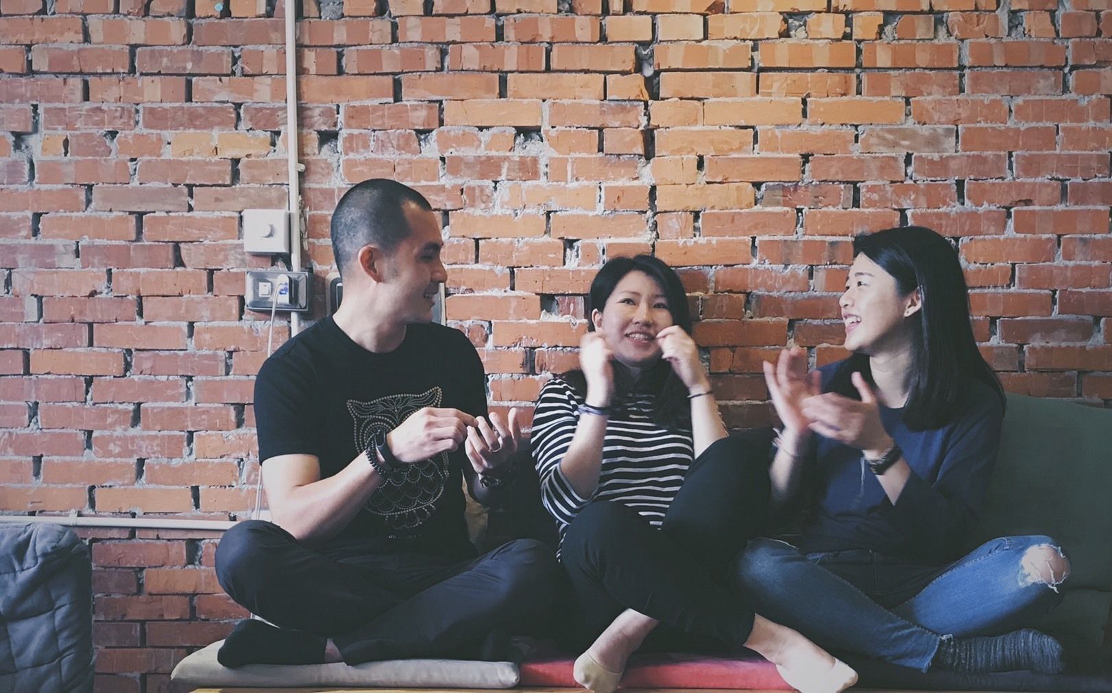 Three people sitting on a couch against a brick wall.