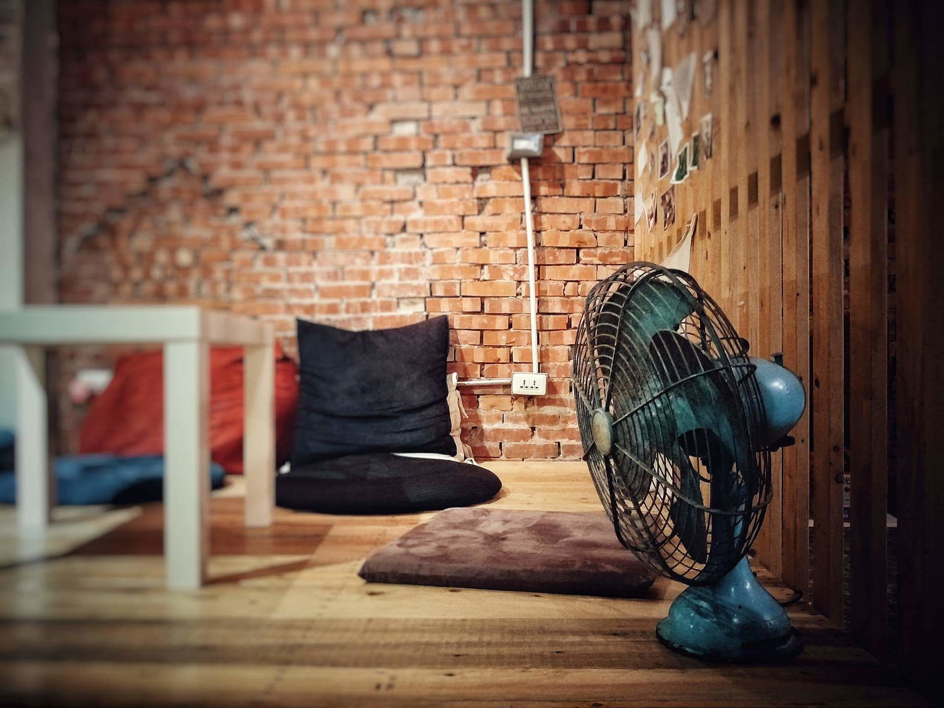 A room with a brick wall, a wooden floor, a blue fan, and a white table.