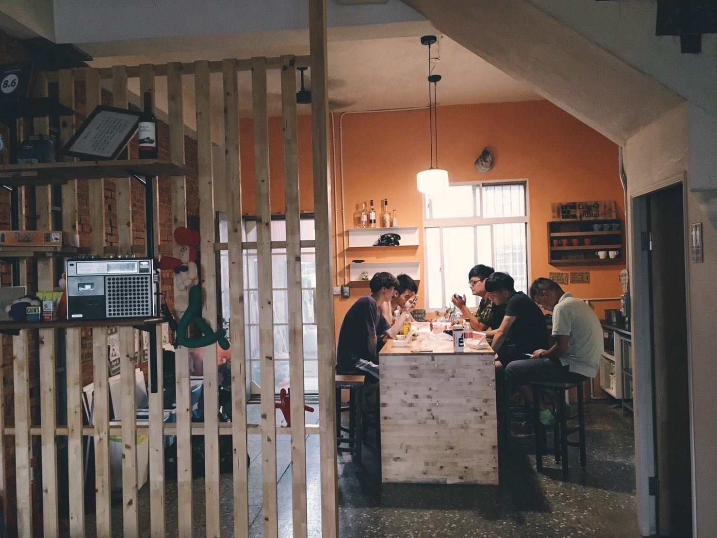 A cozy kitchen with a central island where a group is gathered, surrounded by wooden shelves and a rustic ambiance.