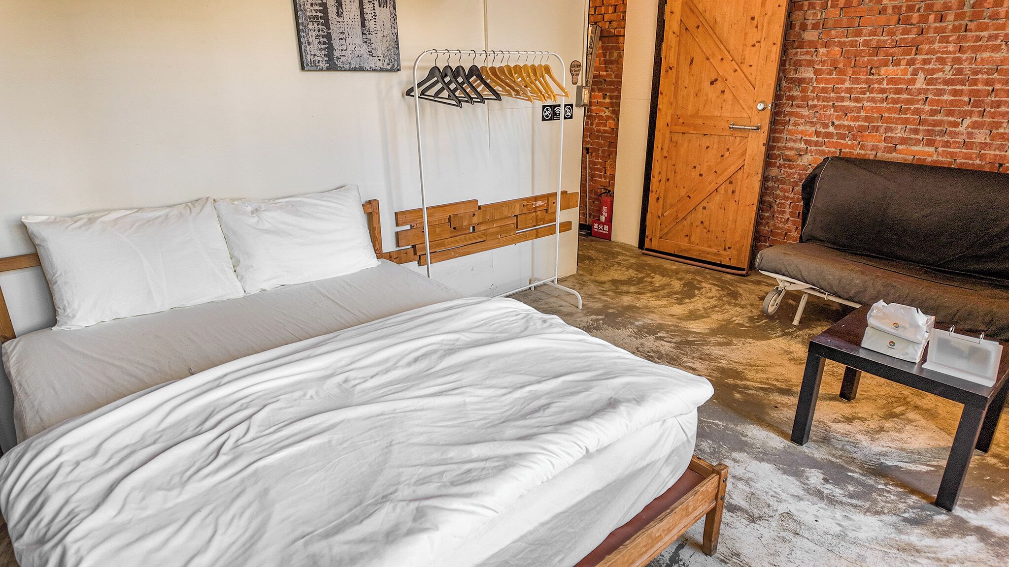 A bedroom with a bed, a wooden bench, a small table, and a clothing rack.