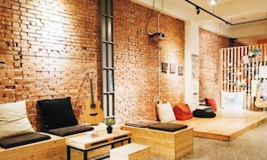 A cozy room with a brick wall, wooden furniture, a guitar, and a small plant. - Lane62 Hostel (Taichung)