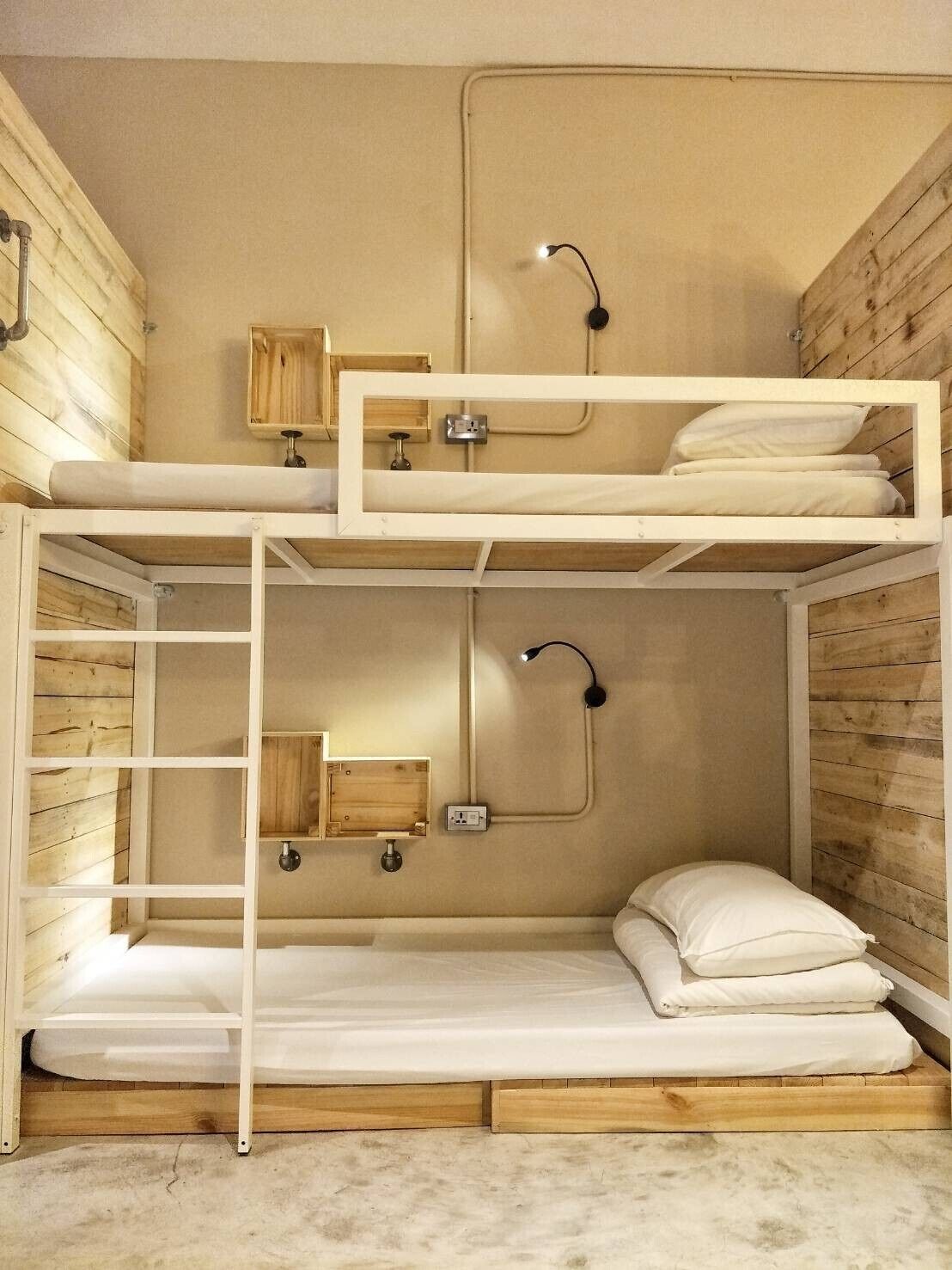 A bunk bed room with a wooden floor, a desk with a lamp, and a shelf with a mirror.