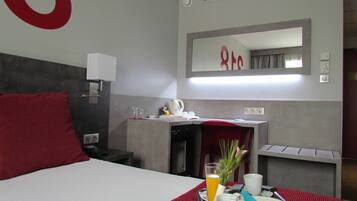 A hotel room with a bed, a desk, a mirror, and a breakfast tray with orange juice, a cup, and pastries.