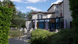 A modern building with outdoor seating and a garden area. - Hôtel L'Hotan (Portet-sur-Garonne)