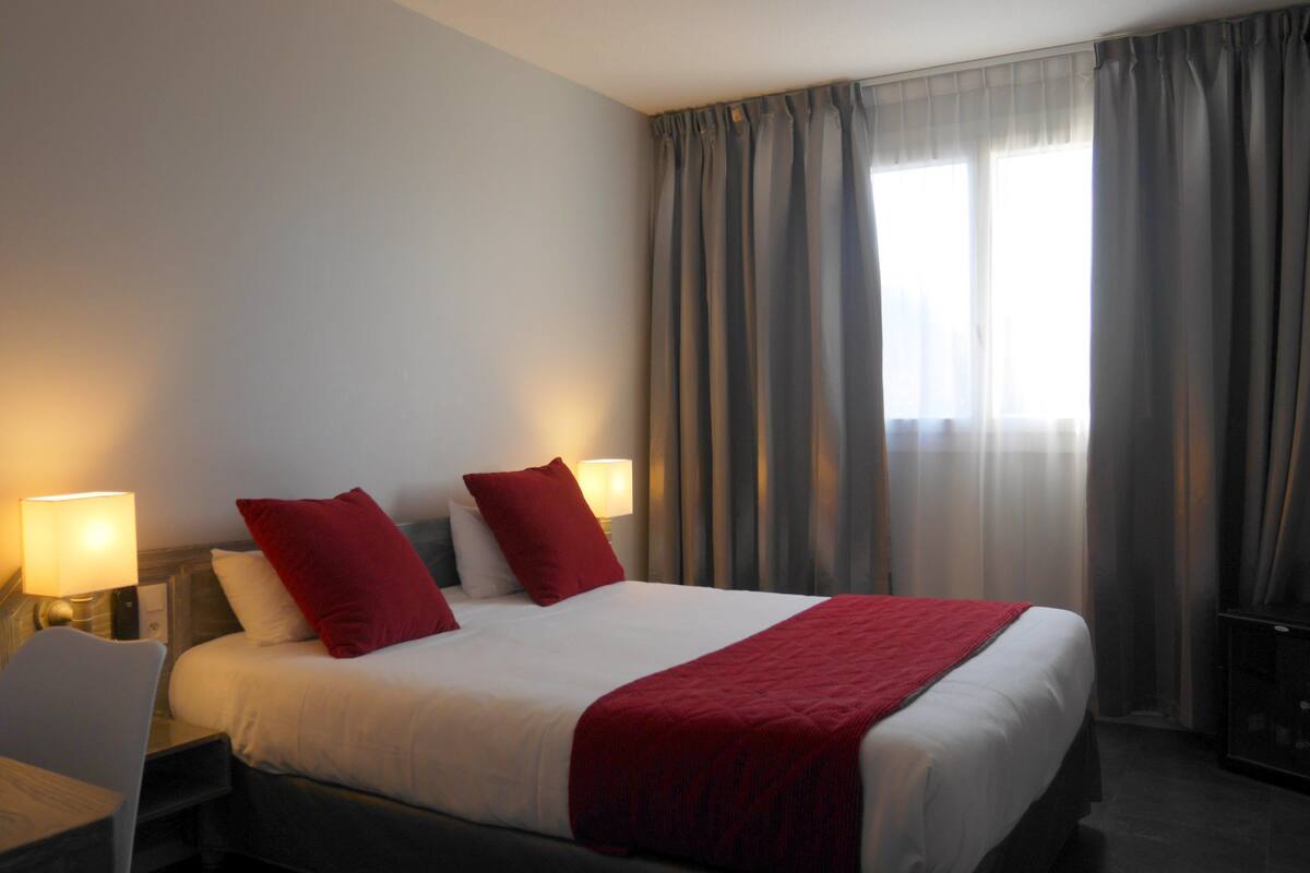 Una habitación de hotel con una cama, dos lámparas de noche, un escritorio y una silla.