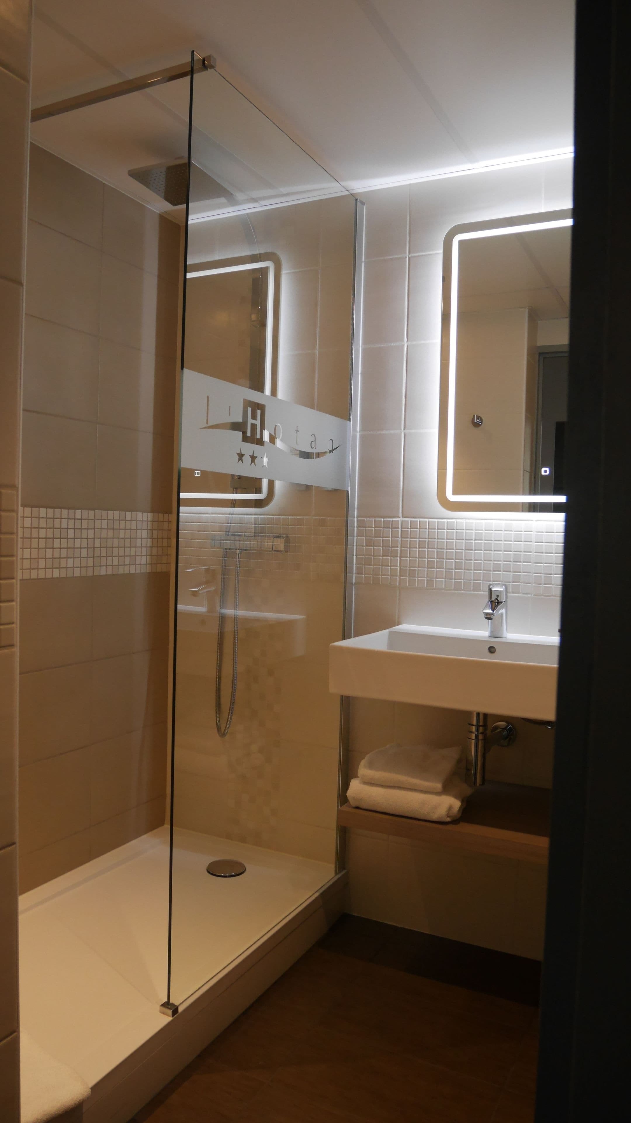 A modern bathroom with a glass-enclosed shower, a white sink, and a mirror above the sink.