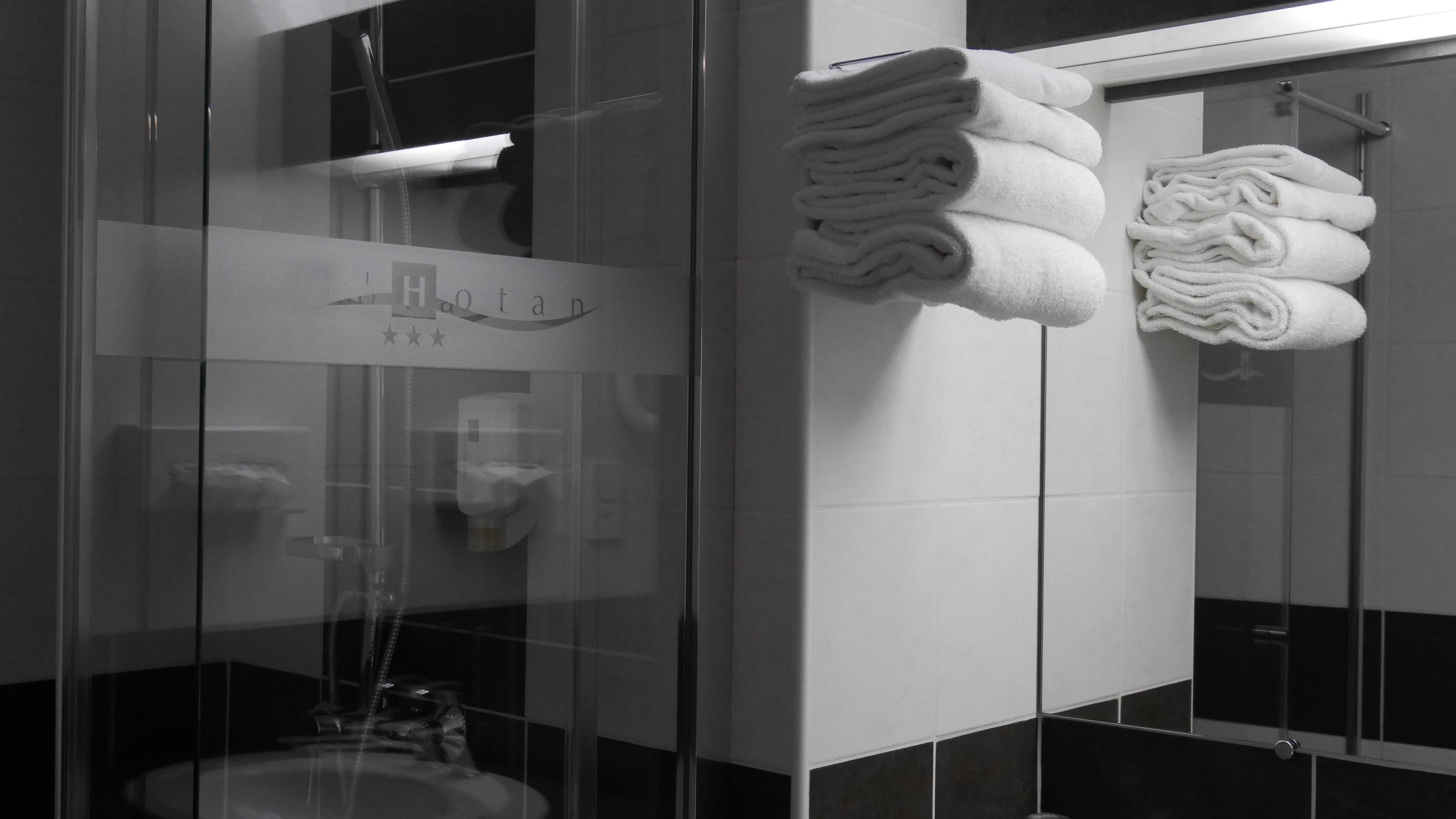 A modern bathroom with a glass shower enclosure, a sink, and neatly stacked towels.