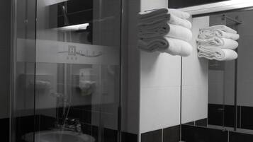 A modern bathroom with a glass shower enclosure, a sink, and neatly stacked towels.