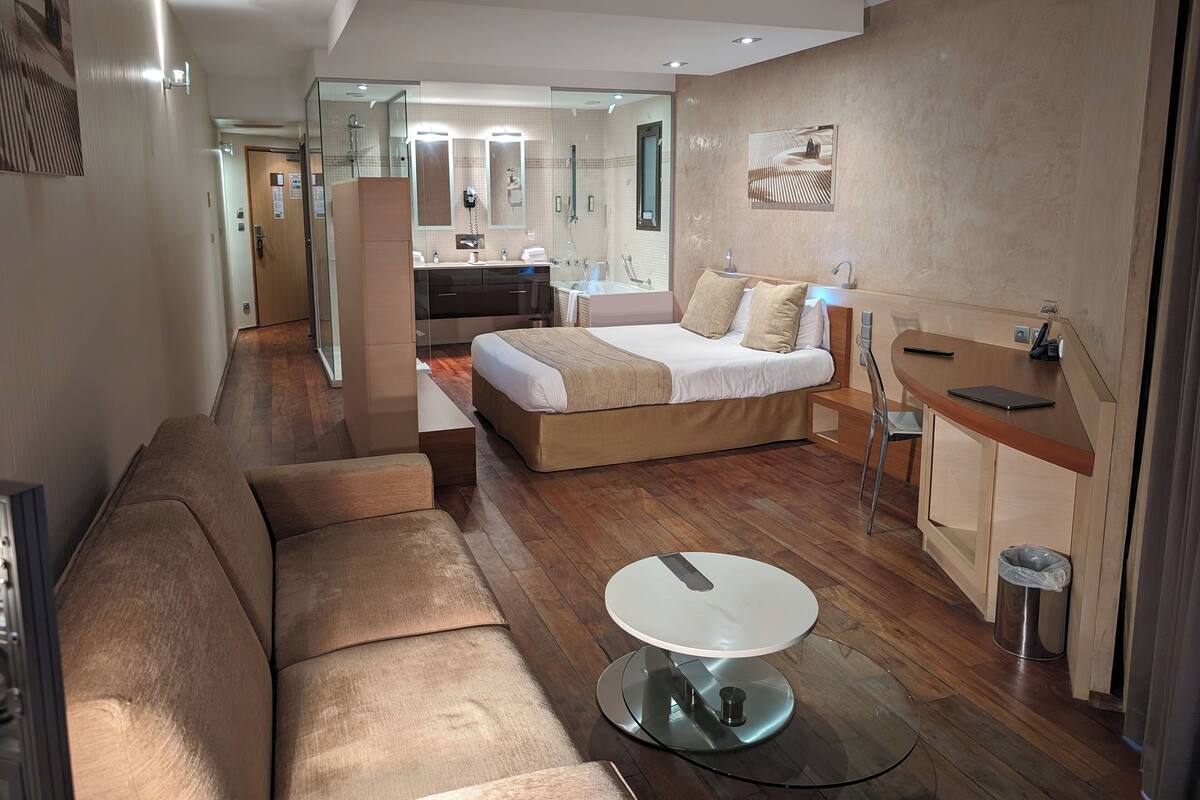 Una habitación de hotel moderna con una cama grande, un sofá, una mesita redonda y una zona de escritorio separada.
