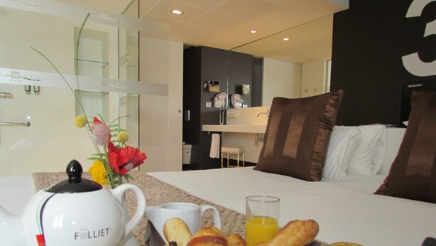 A hotel room with a bed, a breakfast setup including croissants, a teapot, and a vase with flowers. - Hôtel L'Hotan (Portet-sur-Garonne)