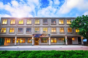 A multi-story hotel with a row of windows on each floor, a storefront with signage, and a well-maintained lawn in front. - The Leaf Inn (Hualien City)