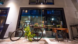 A bicycle parked in front of a building with a large window, a sewing machine, and a small table with a plant. - The Leaf Inn (Hualien City)