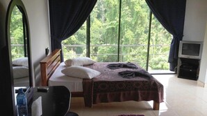 A bedroom with a bed, a desk, a mirror, a TV, and large windows with curtains. - Kandy View Hotel (Kandy)