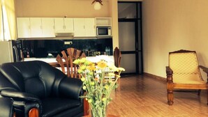 A living room with a black leather sofa, a wooden dining table with chairs, and a vase of flowers. - Kandy View Hotel (Kandy)