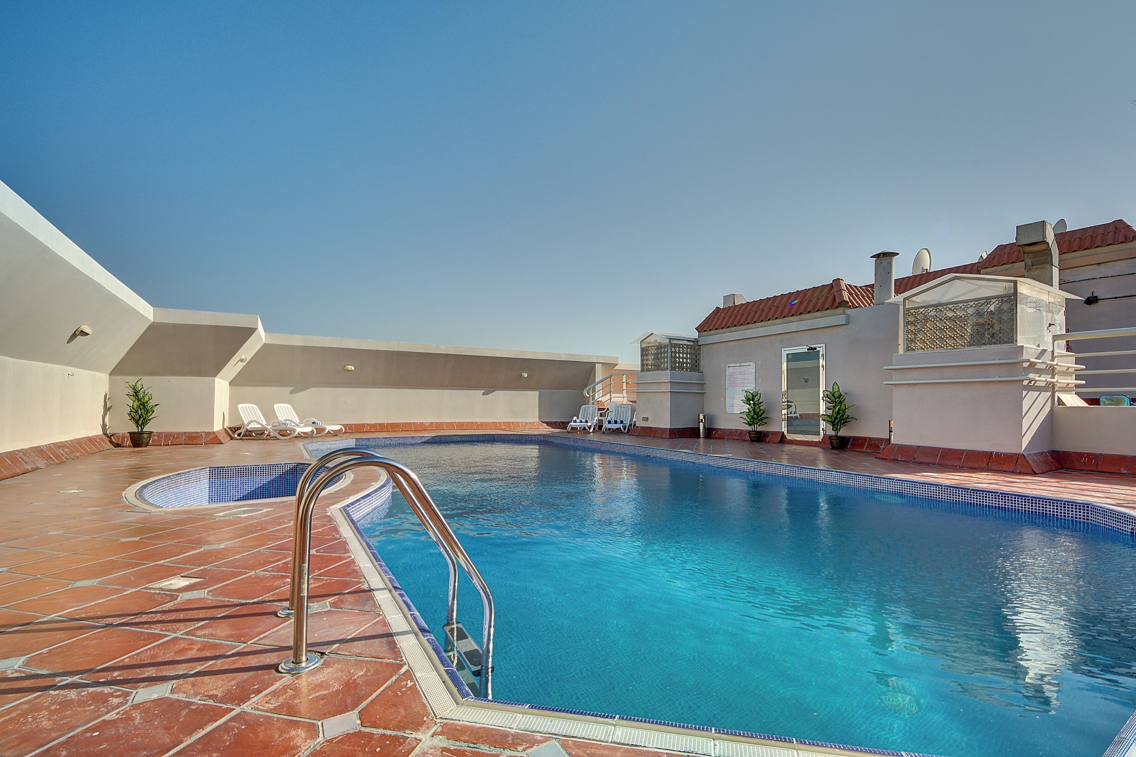 A swimming pool with a tiled deck, lounge chairs, and a building with a red roof.