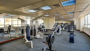 Un gimnasio con diferentes máquinas de ejercicio, ventanas amplias y un muro espejado.