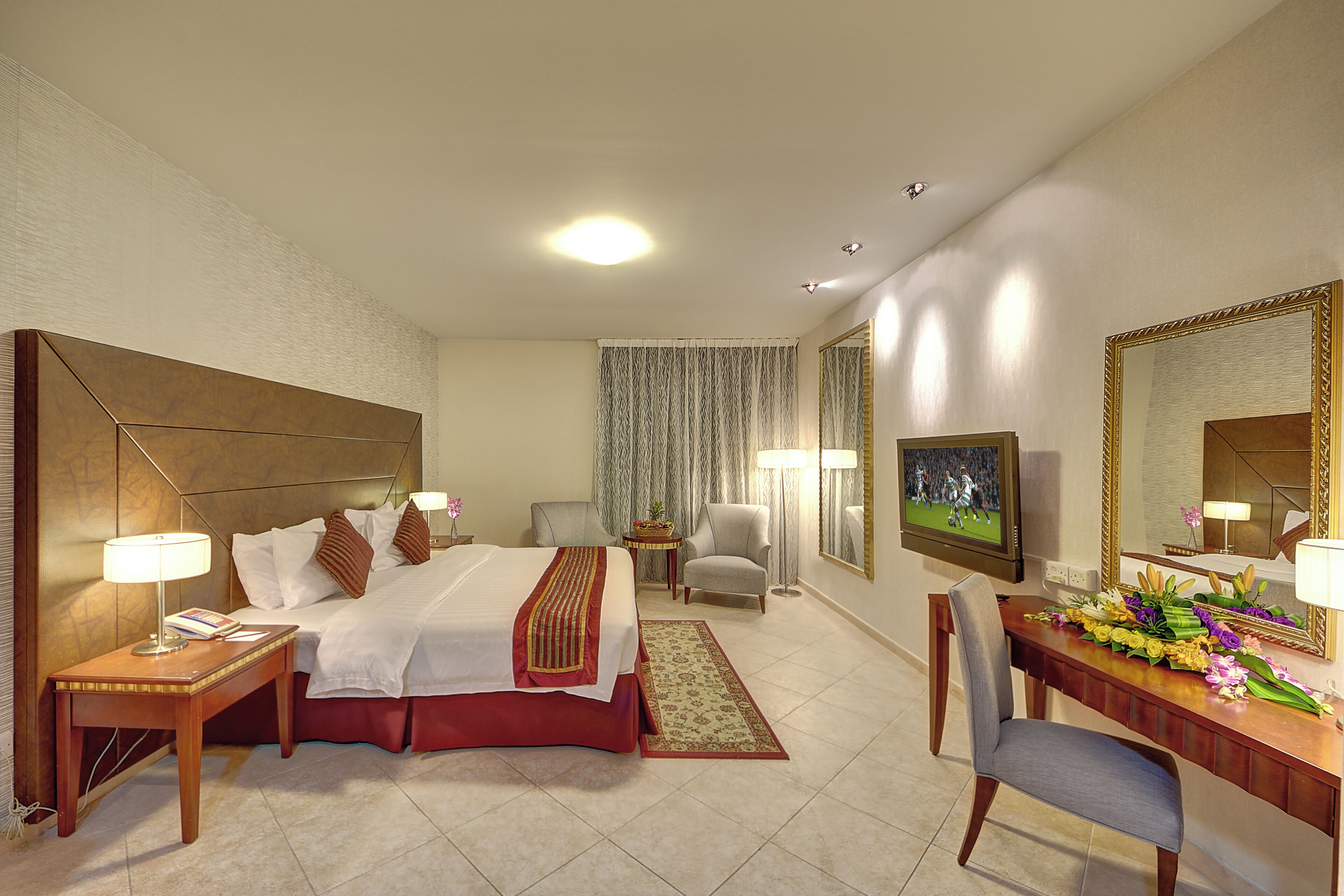 A hotel room with a large bed, a desk, a chair, a television, and a mirror.