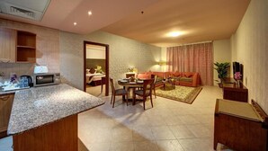 Un espacio habitable compacto con kitchenette, comedor y zona de estar con sofá y sillones.