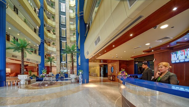 Un vestíbulo de hotel con suelo de mármol, varios pisos, un mostrador de recepción y plantas de interior.