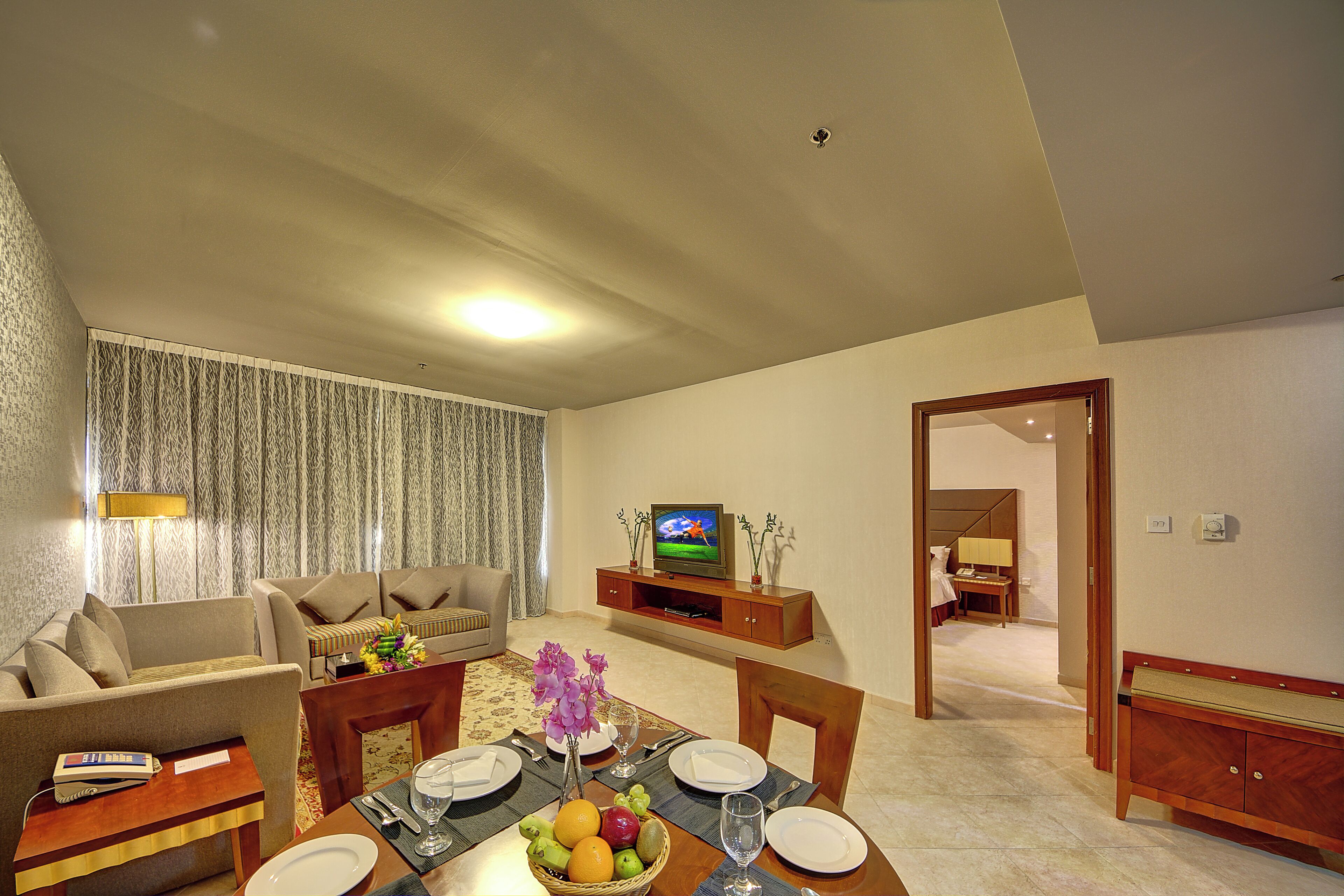 A living room with a sofa, a dining table set for four, a television, and a hallway leading to another room.