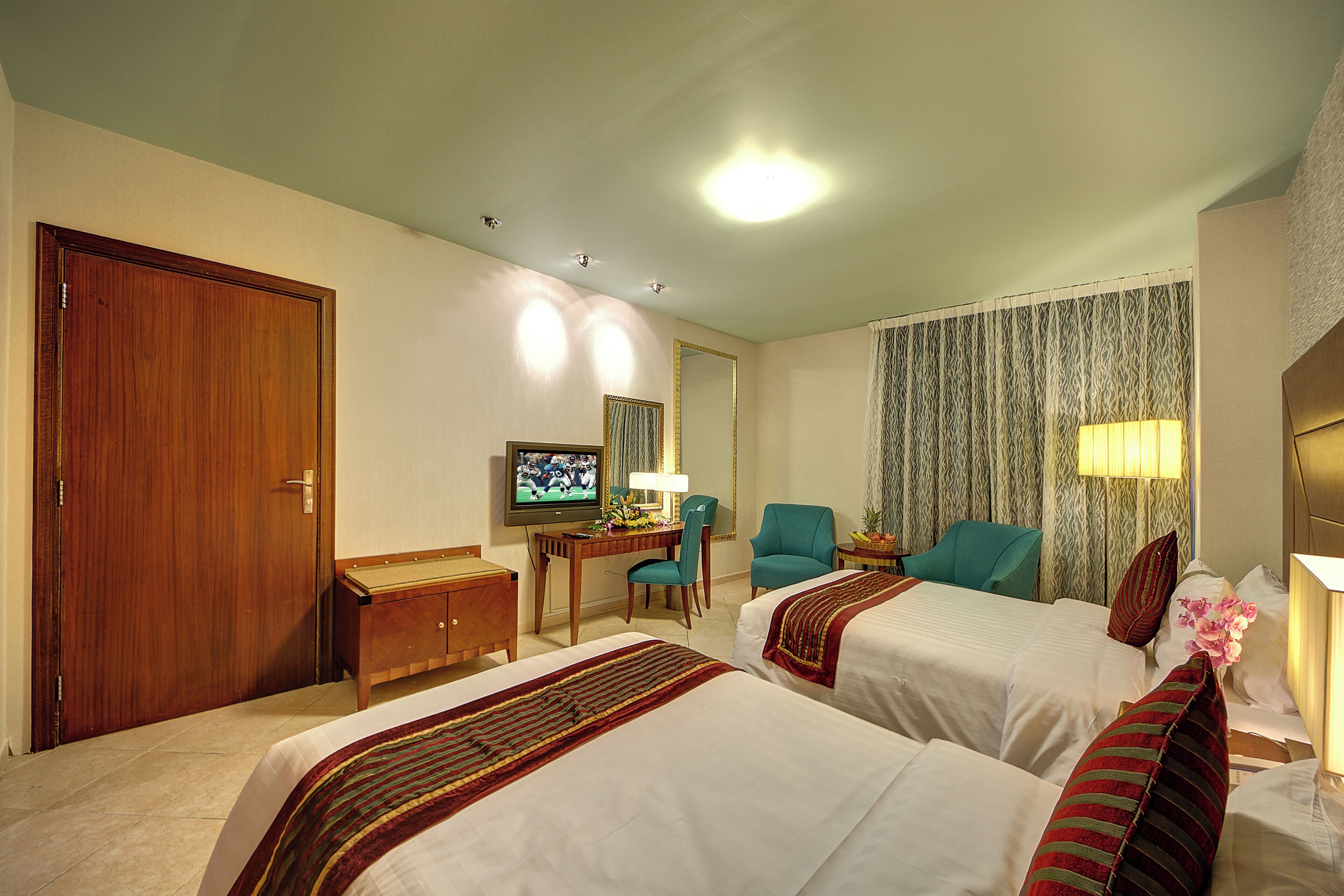 A hotel room with two beds, a desk with a television, a chair, and a window with curtains.