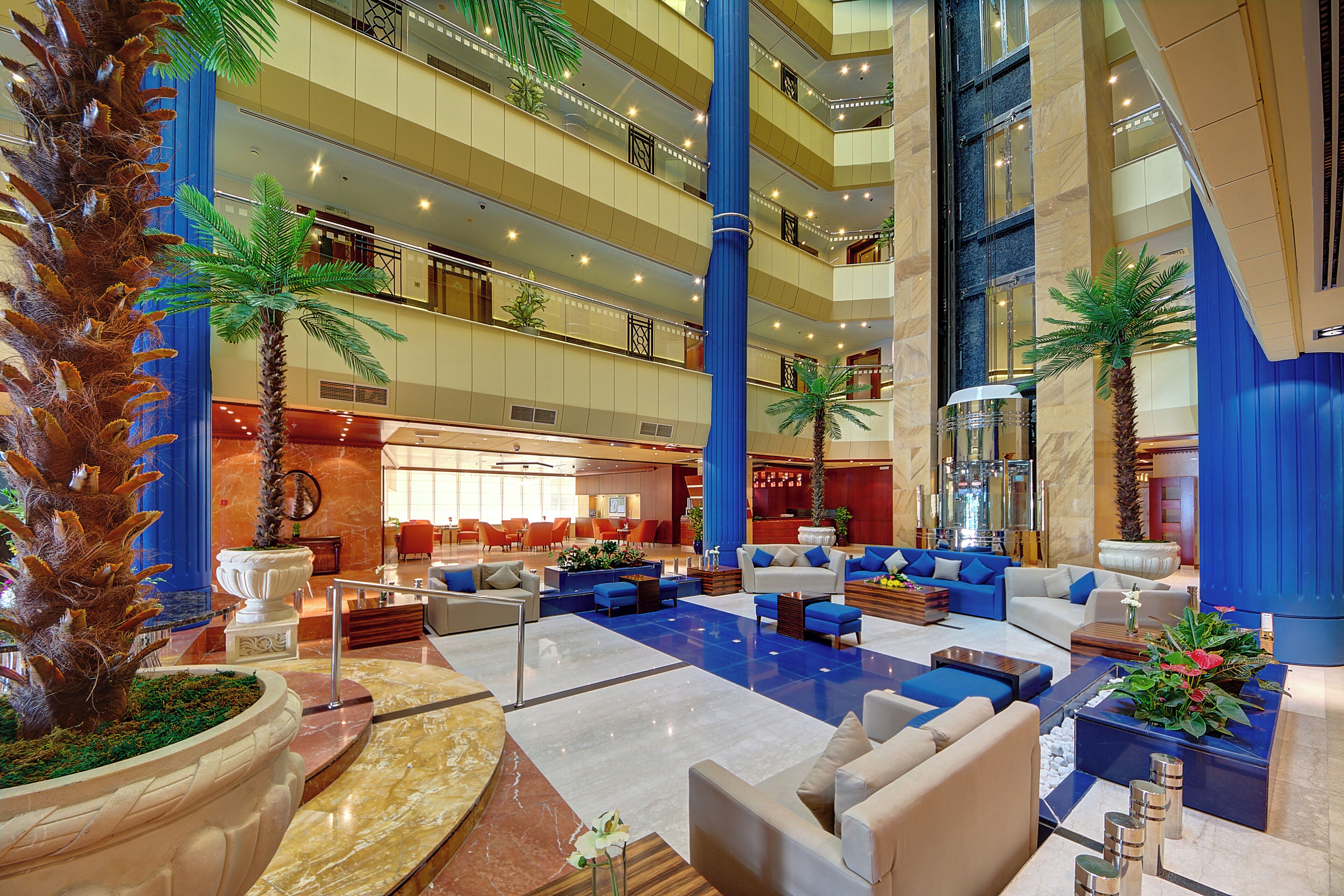 A multi-level hotel lobby with a central atrium, multiple seating areas, and decorative palm trees.