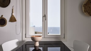 A dining area with a table, chairs, a bowl, and a view of the sea through a window. - Ianemi Suites by K4 Kythnos (Kithnos)