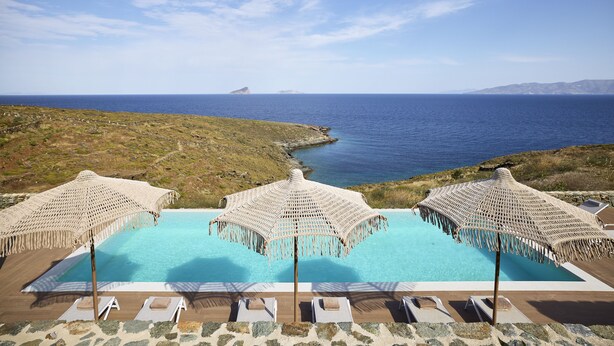 A pool area with three woven umbrellas, lounge chairs, and a view of the sea and distant island. - Ianemi Suites by K4 Kythnos (Kithnos)