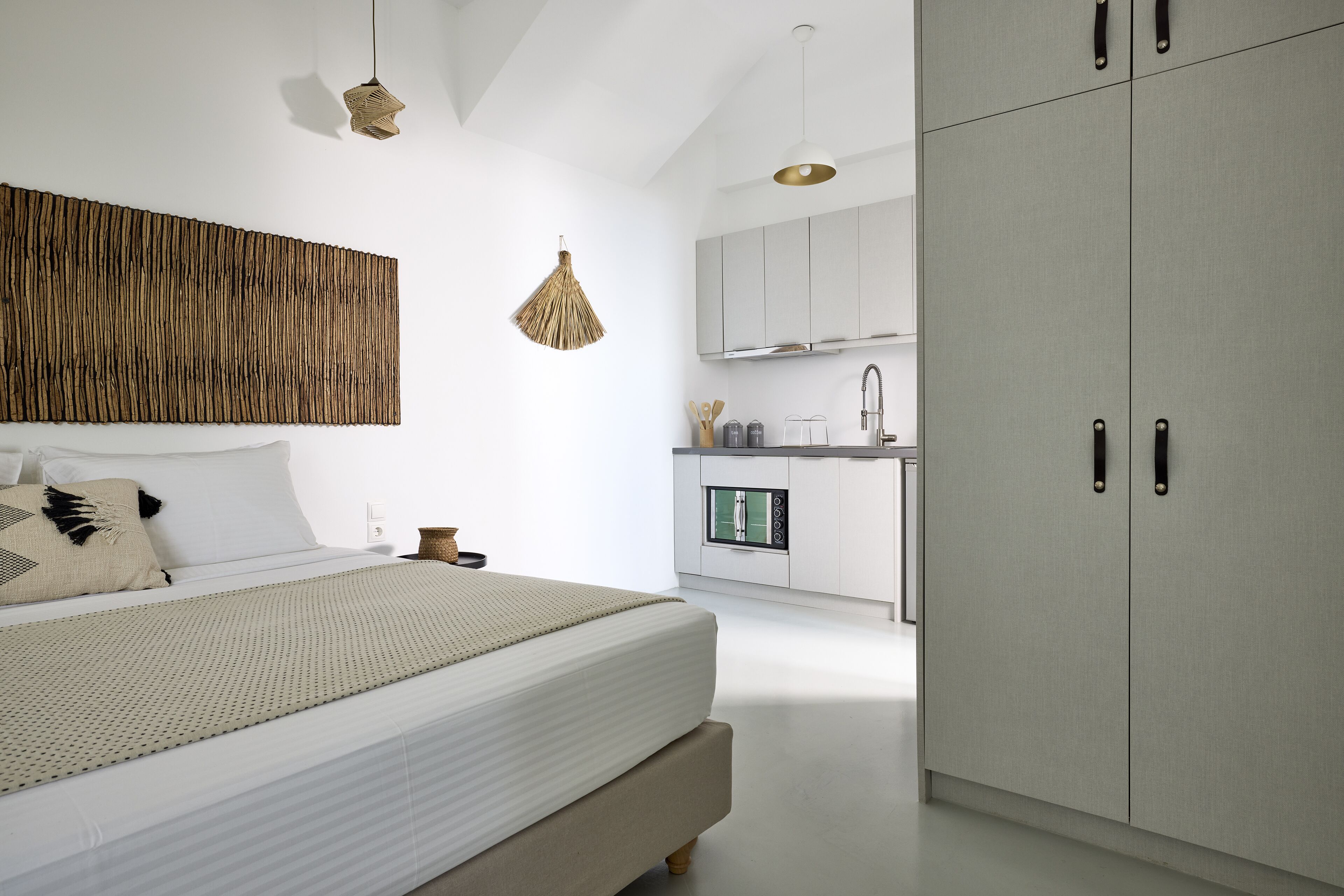 A modern bedroom with a large bed, a wooden wall art piece, and a kitchen area with cabinets and a sink.