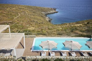 A pool area with two umbrellas and lounge chairs, overlooking a rocky coastline.