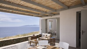 A terrace with a view of the sea, furnished with white chairs and a table, and a wicker chair. - Ianemi Suites by K4 Kythnos (Kithnos)