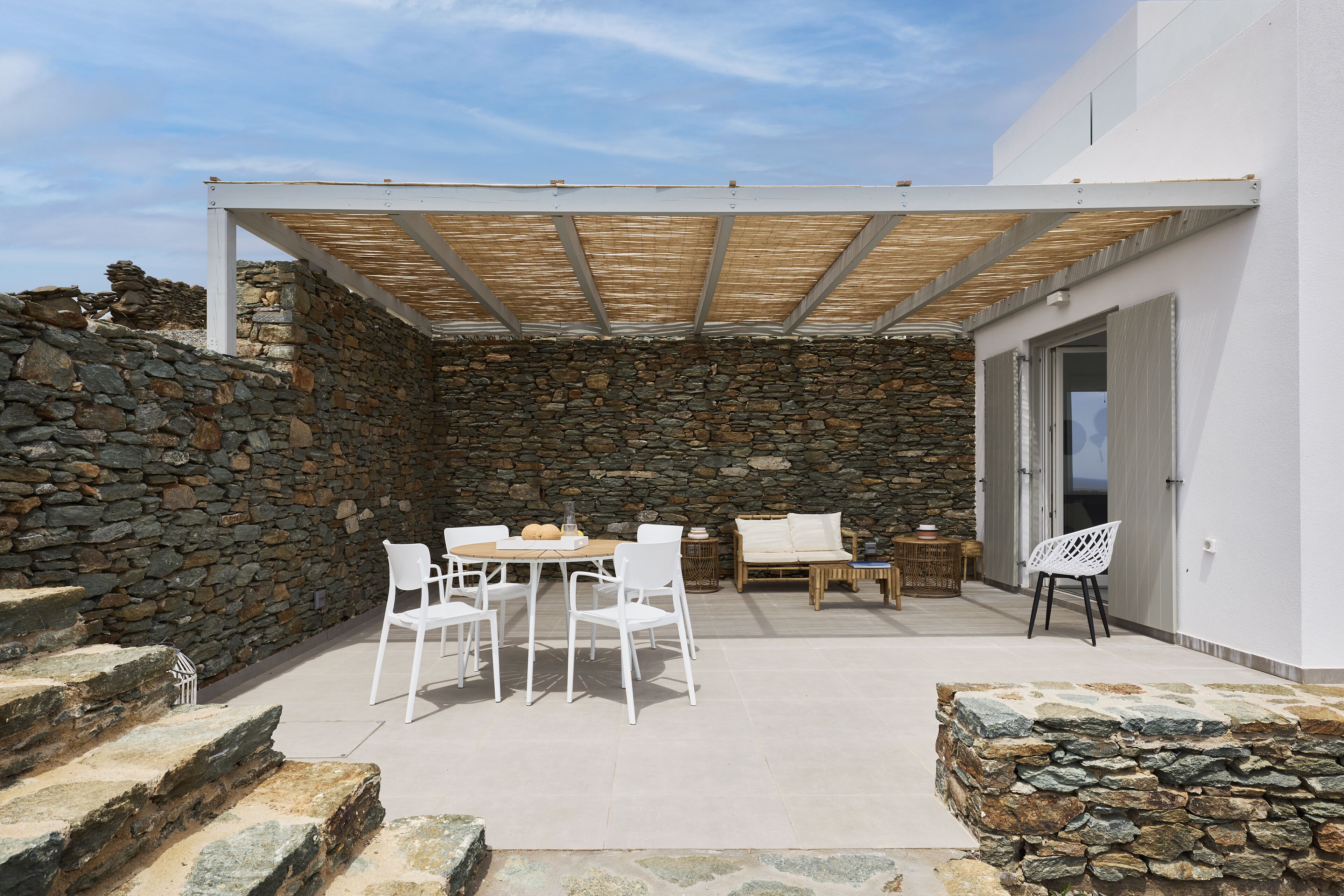 A covered patio with stone walls, white furniture, and a wooden table.