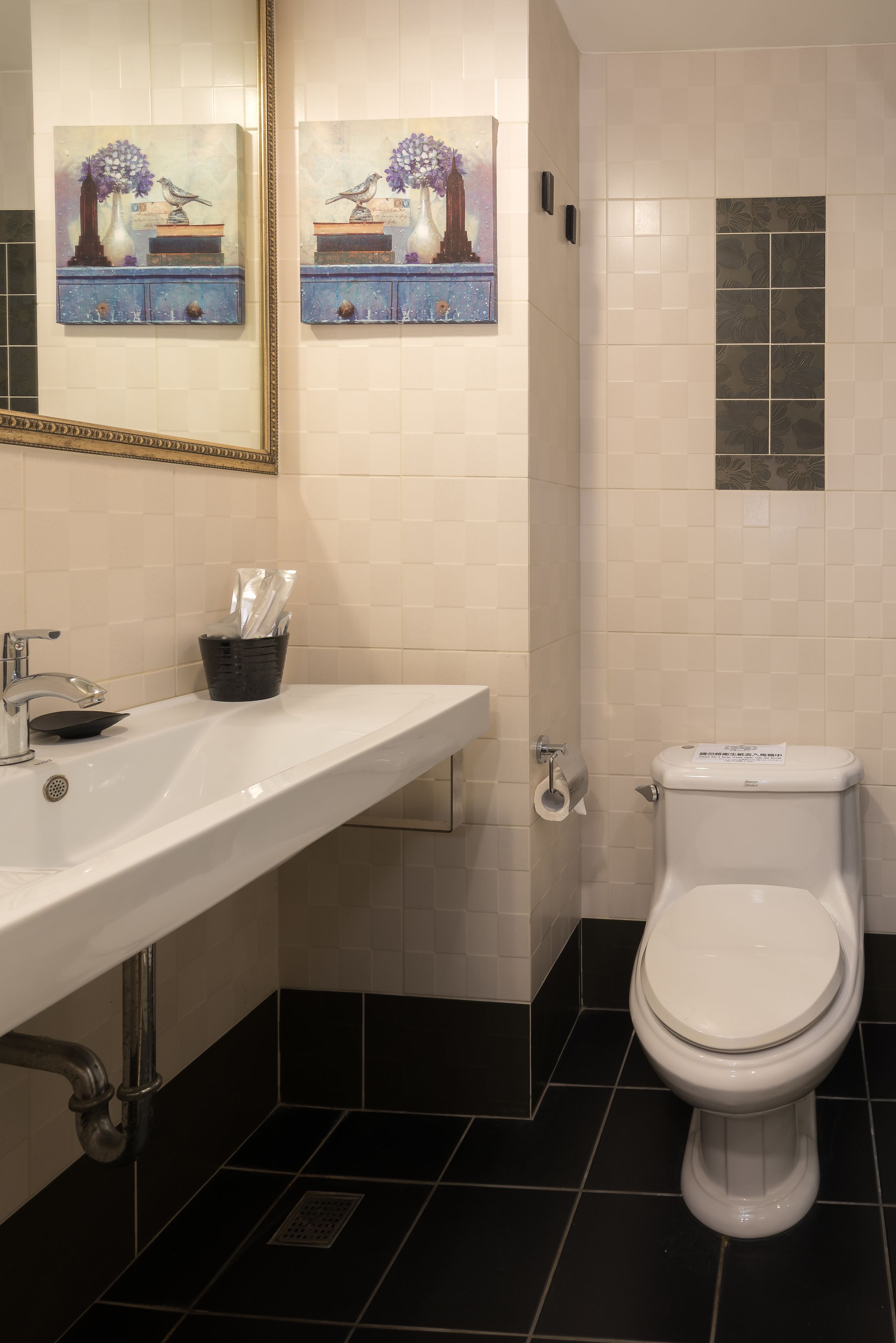A bathroom with a white sink, black tiled floor, a toilet, and two paintings on the wall.