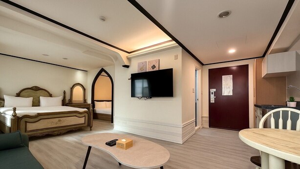 Habitación de hotel con cama, televisor montado en la pared, una mesita, una silla y una puerta que da al baño.