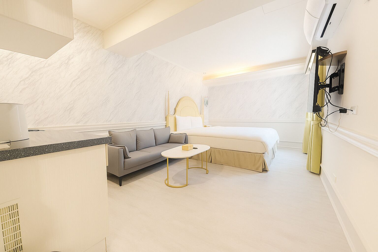A modern hotel room with a sofa, a small round table, a bed, and a TV mounted on the wall.