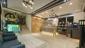 Un hall de hotel con mostrador de recepción, escalera, zona de estar y máquina expendedora.