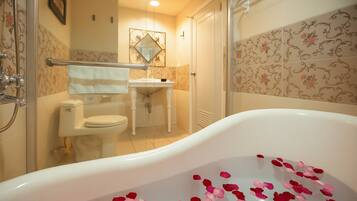 A bathroom with a bathtub filled with rose petals, a toilet, and a shower area.