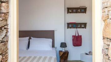 A bedroom with a bed, a nightstand, a lamp, a red bag, and a wall-mounted shelf.