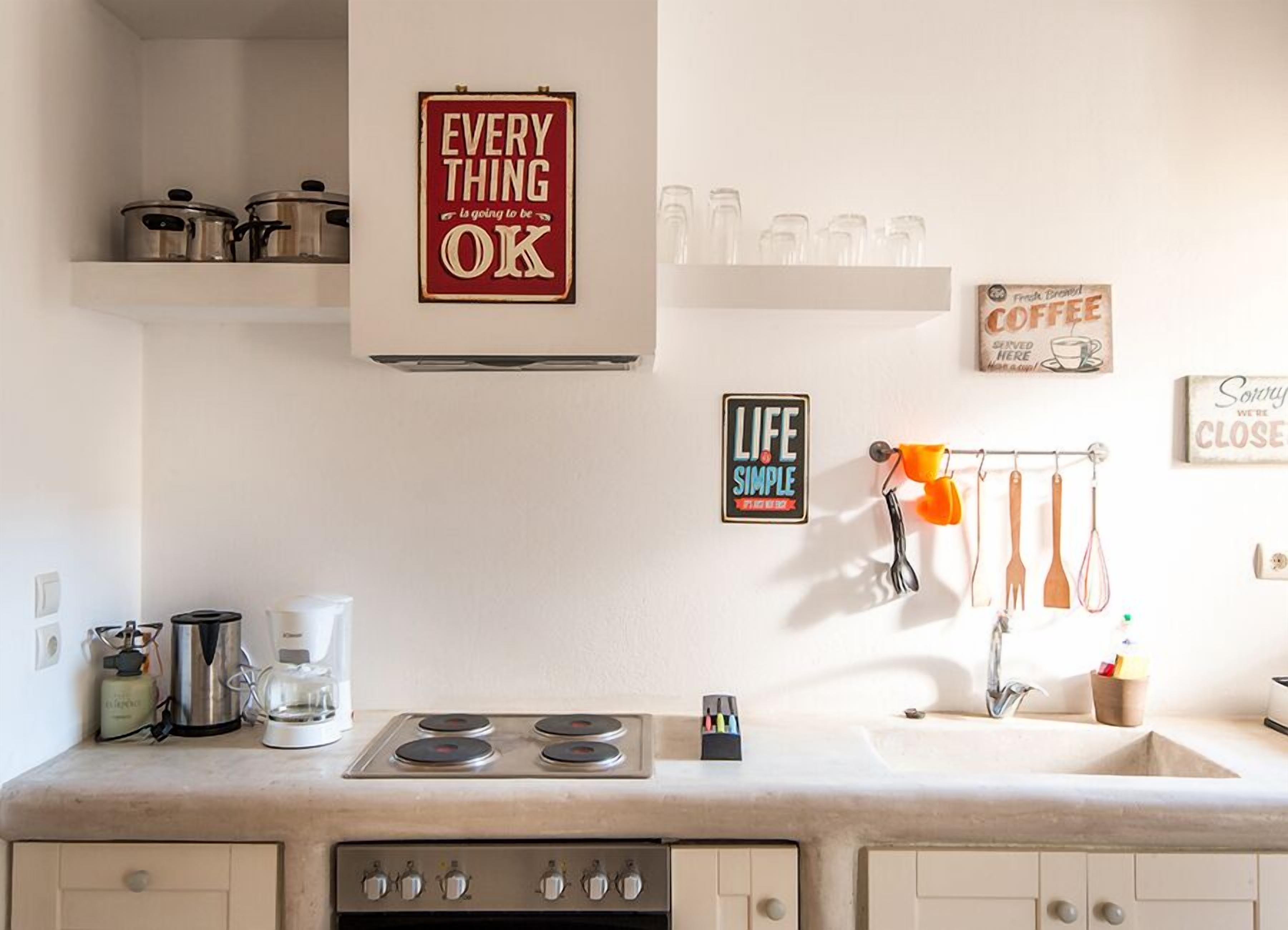 Eine Küche mit Herd, Kaffeemaschine und verschiedenen Küchengeräten. An den Wänden befinden sich Schilder, darunter eines mit der Aufschrift 'Everything is going to be OK'.