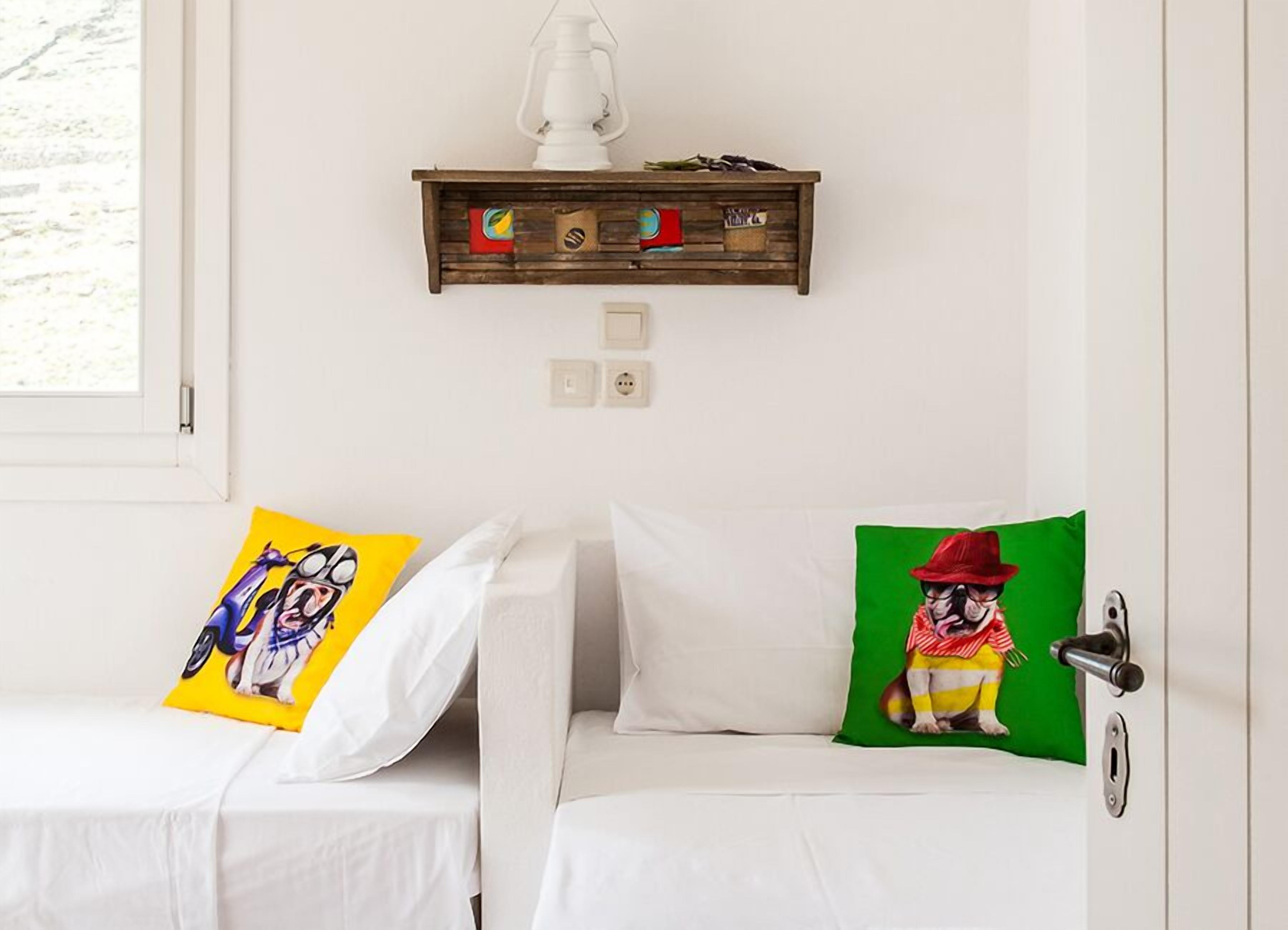 A room with two white beds, each with a colorful pillow. A wooden shelf with a white lantern hangs above the beds.