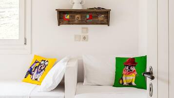 A room with two white beds, each with a colorful pillow. A wooden shelf with a white lantern hangs above the beds.