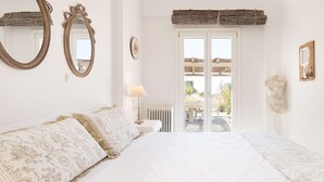 Ein Schlafzimmer mit einem großen Bett, zwei Wandspiegeln, einer Nachttischlampe und Blick durch eine Glastür in einen Außenbereich.