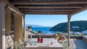 Ein Sitzbereich im Freien mit Tisch und Stühlen, mit Blick auf eine Küstenlandschaft und Meer sowie Hügel.