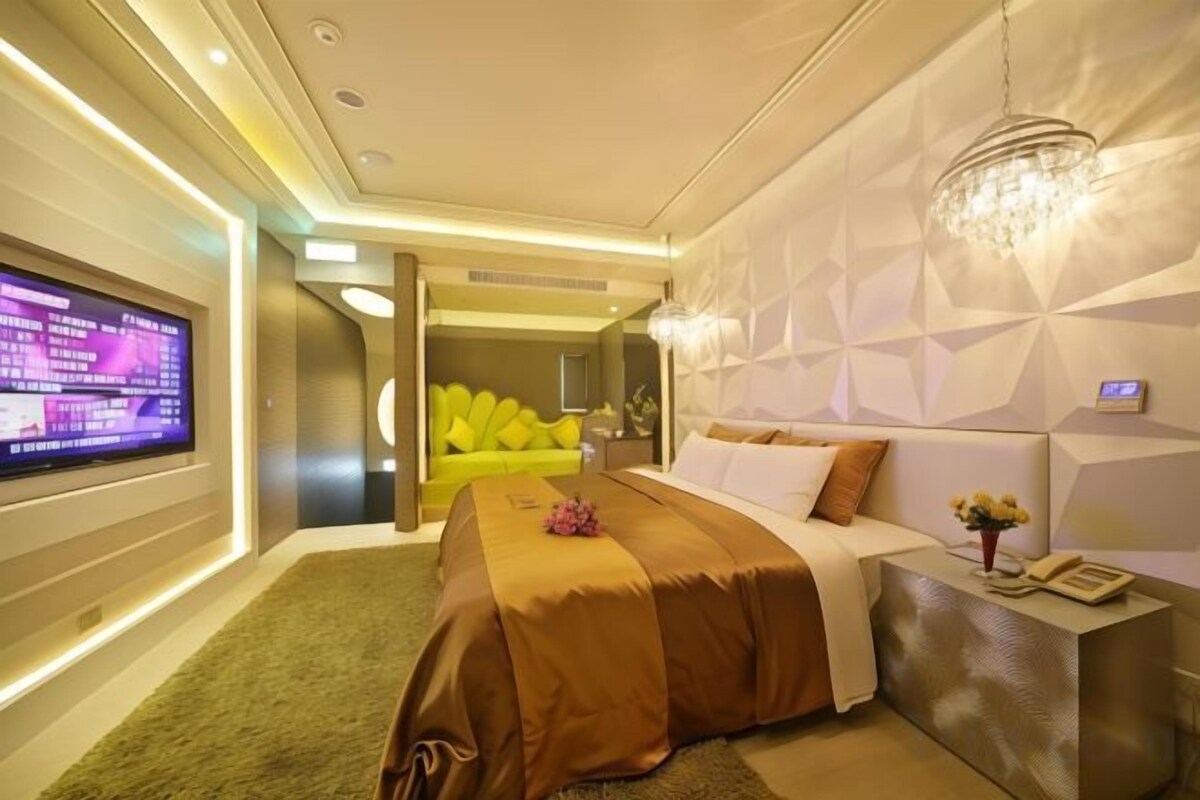 Habitación de hotel moderna con una cama grande, televisión y una pared de acento amarillo brillante.