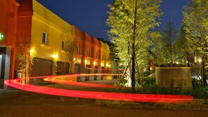 Ein Gebäude mit gelber Fassade und rotem Dach, umgeben von Bäumen und einer gepflasterten Fläche.