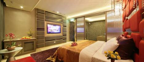 Una habitación de hotel moderna con una cama grande, un televisor, una zona de estar con un sofá rojo y una pequeña mesa con una planta.