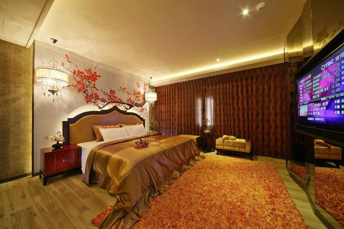 A hotel room with a large bed, a TV, a red cabinet, and a decorative wall piece.
